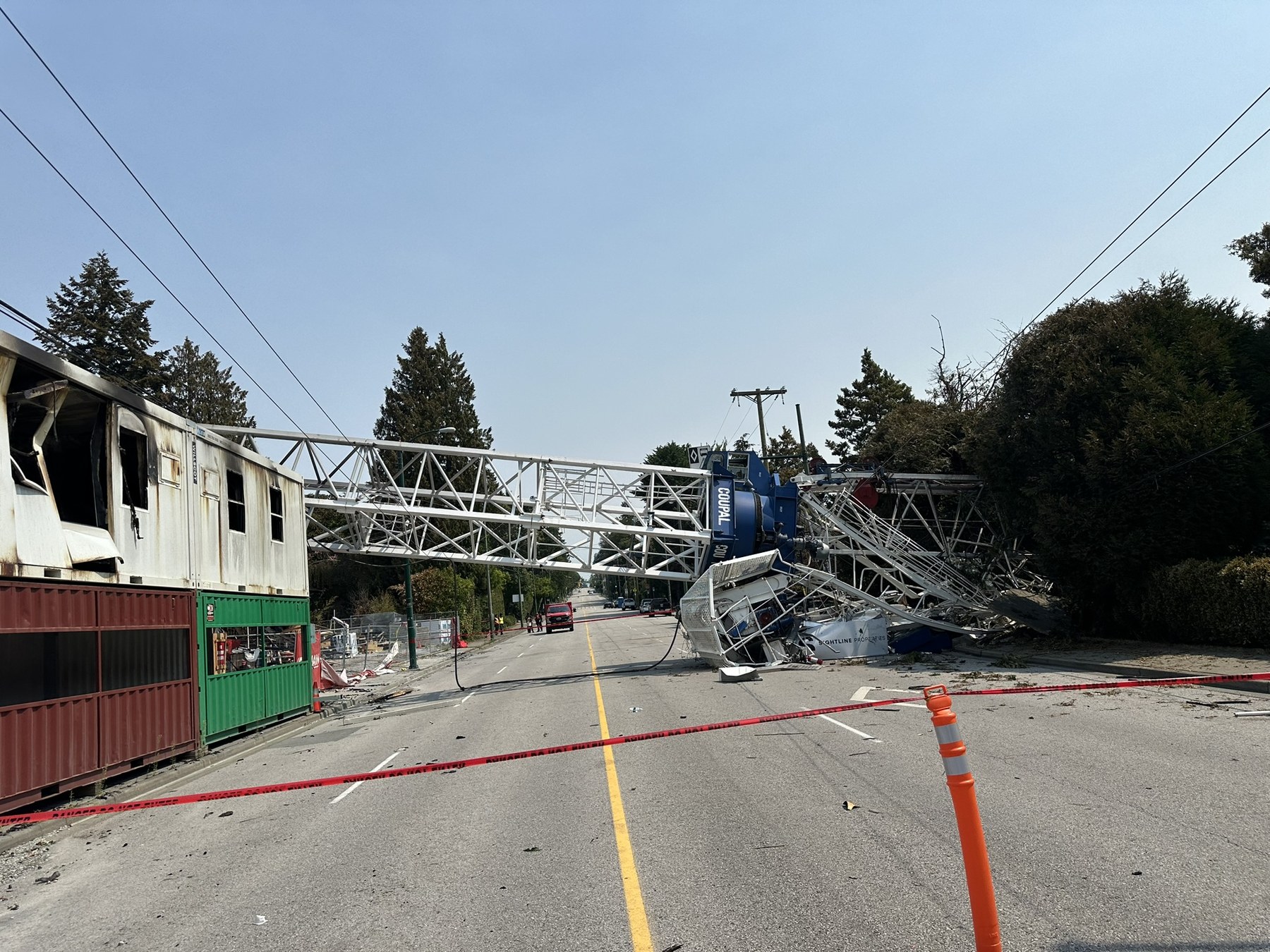 Wide view of collapsed tower crane spanning the street beside a fire-damaged construction site