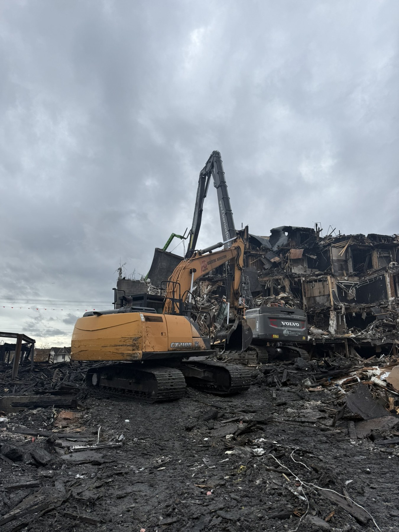 High-reach demolition equipment working beside the fire-damaged Langley construction site