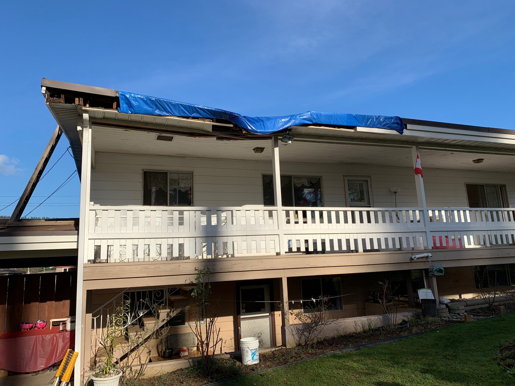 Residential roof and exterior damage temporarily covered with blue tarping after a tree impact event